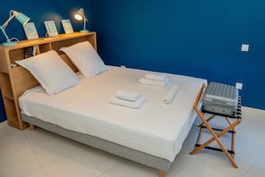 A neatly made bed with white linens, a set of folded towels, and a suitcase on a wooden stand.