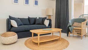 Ein modernes Wohnzimmer mit einem dunkelblauen Sofa, einem Holztisch, einem gewebten Pouf und einem Korbstuhl.