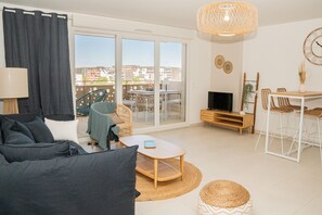 A modern living room with a sofa, a TV stand, and a dining area with chairs and a table. - Sète, Apt 2 chambres, Terrasse et proximité plages (Sète)