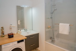 A modern bathroom with a glass-enclosed shower, a sink with a mirror, and a washing machine.
