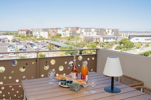 A balcony with a table set for a meal, including wine glasses, a bottle, and a loaf of bread.