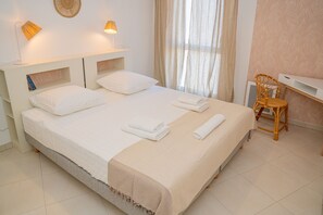 A neatly made bed with white linens, a bedside lamp, and a chair with a woven backrest.