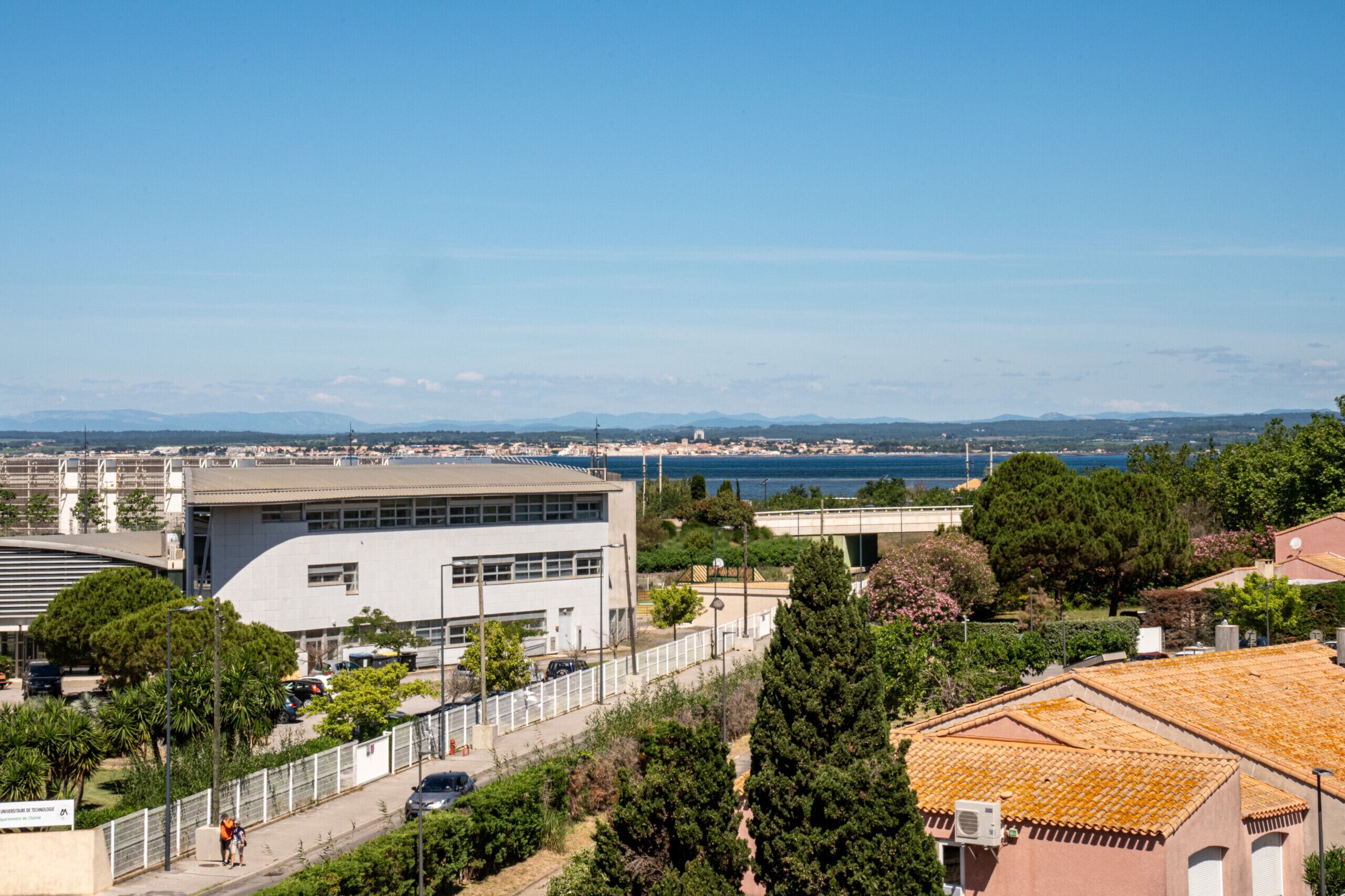A coastal cityscape with modern buildings, a clear blue sky, and a view of the sea.