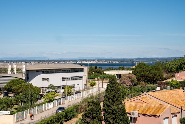 A coastal cityscape with modern buildings, a clear blue sky, and a view of the sea.