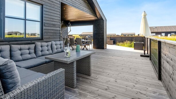 Una terraza moderna al aire libre con sofá y mesa, piso de madera y vistas del entorno.