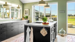 Una cocina moderna con una isla grande, luces colgantes y vistas al campo.