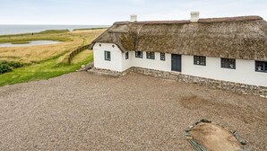A white house with a thatched roof, situated on a gravel driveway with a view of the sea and grassy fields. - "Vili" - 100m from the sea by Interhome (Lemvig)