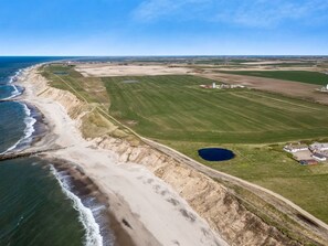 Oversigtsbillede af et kystområde med en strand, grønne marker og et mindre vandareal.