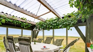 A covered outdoor dining area with a table and chairs, surrounded by large windows offering a view of the countryside. - "Vili" - 100m from the sea by Interhome (Lemvig)