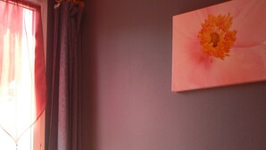 A bedroom with a bed, a window with curtains, and a painting on the wall.