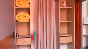 A hotel room with a wooden wardrobe, a bed, a bedside table, and a curtain.
