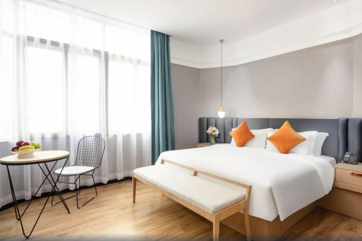 Ein modernes Hotelzimmer mit einem großen Bett, einem Nachttisch, einem Sessel, einem kleinen Tisch mit Früchten und einer Bank.