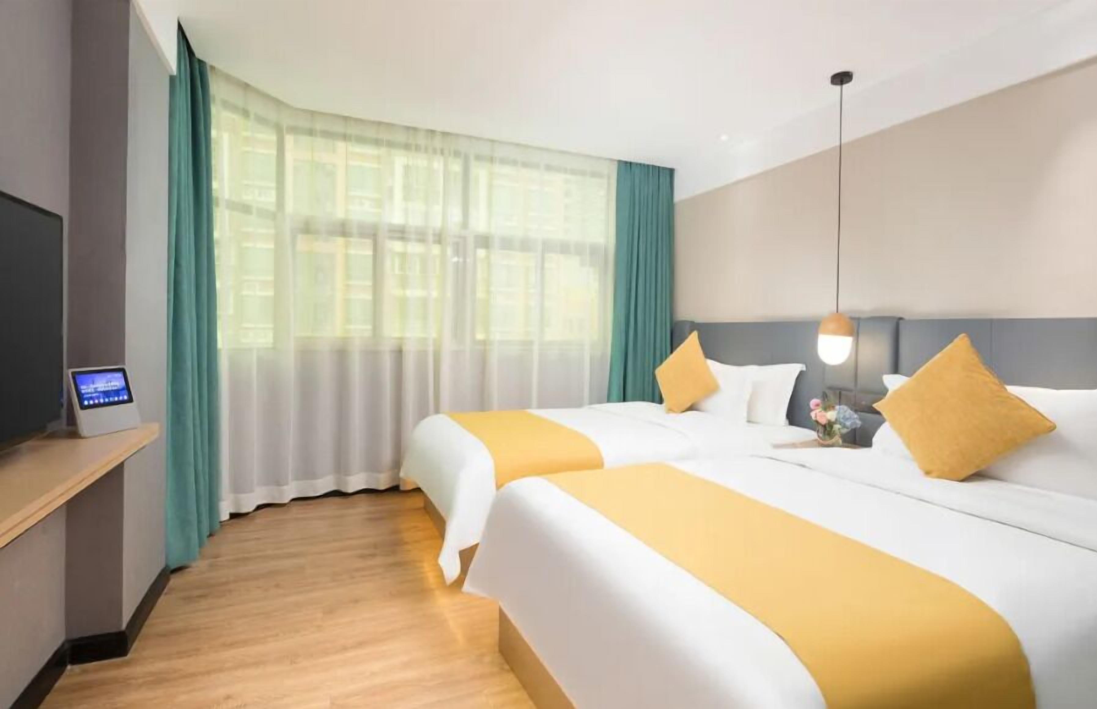 A hotel room with two beds, a TV on a stand, and a window with curtains.