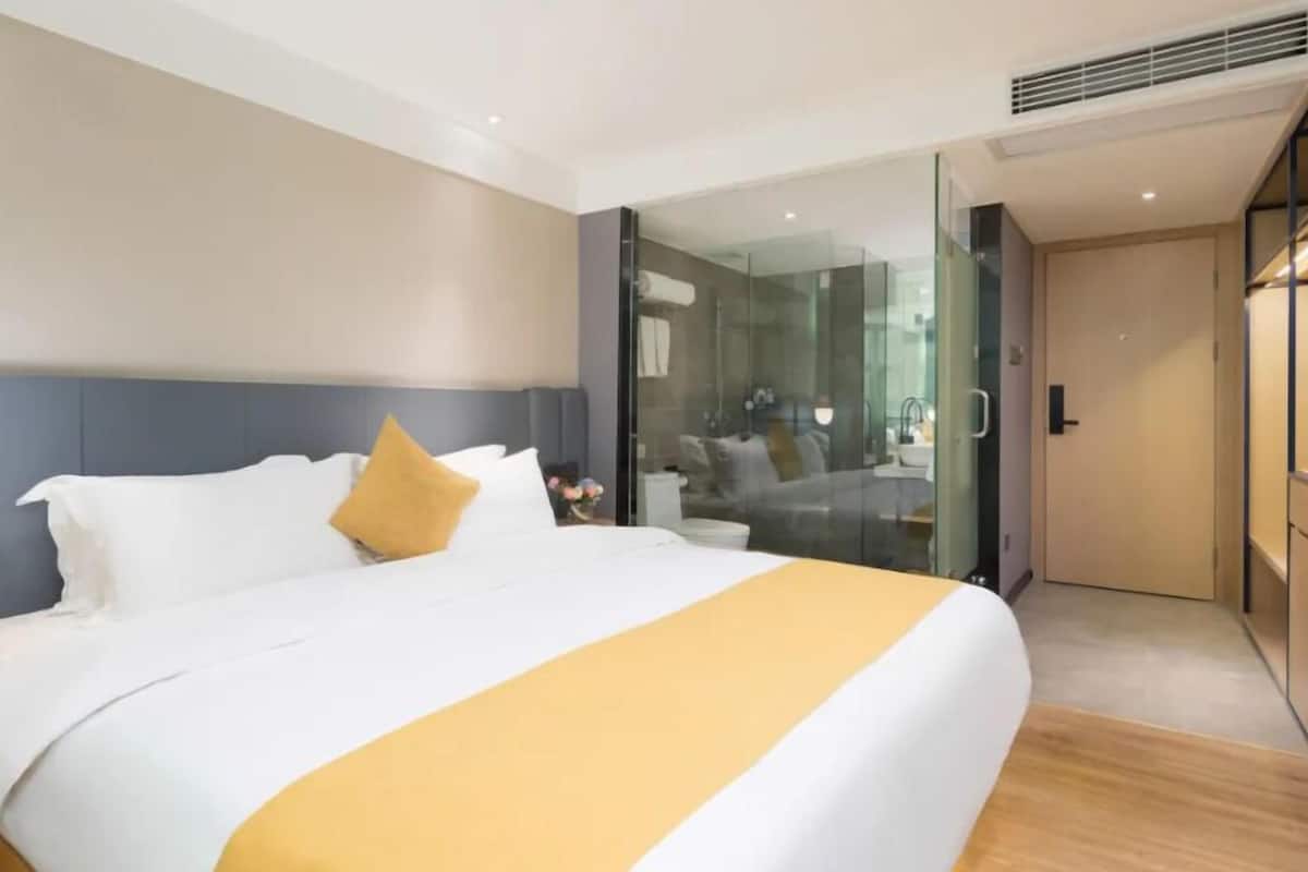 Ein modernes Hotelzimmer mit einem großen Bett, einer Duschkabine aus Glas und Holzboden.