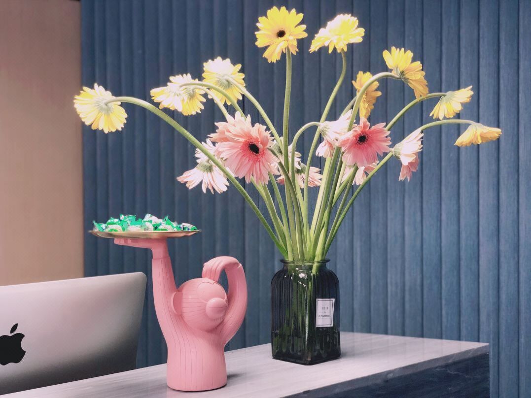 A desk with a laptop, a pink flamingo-shaped vase, and a green vase with flowers.