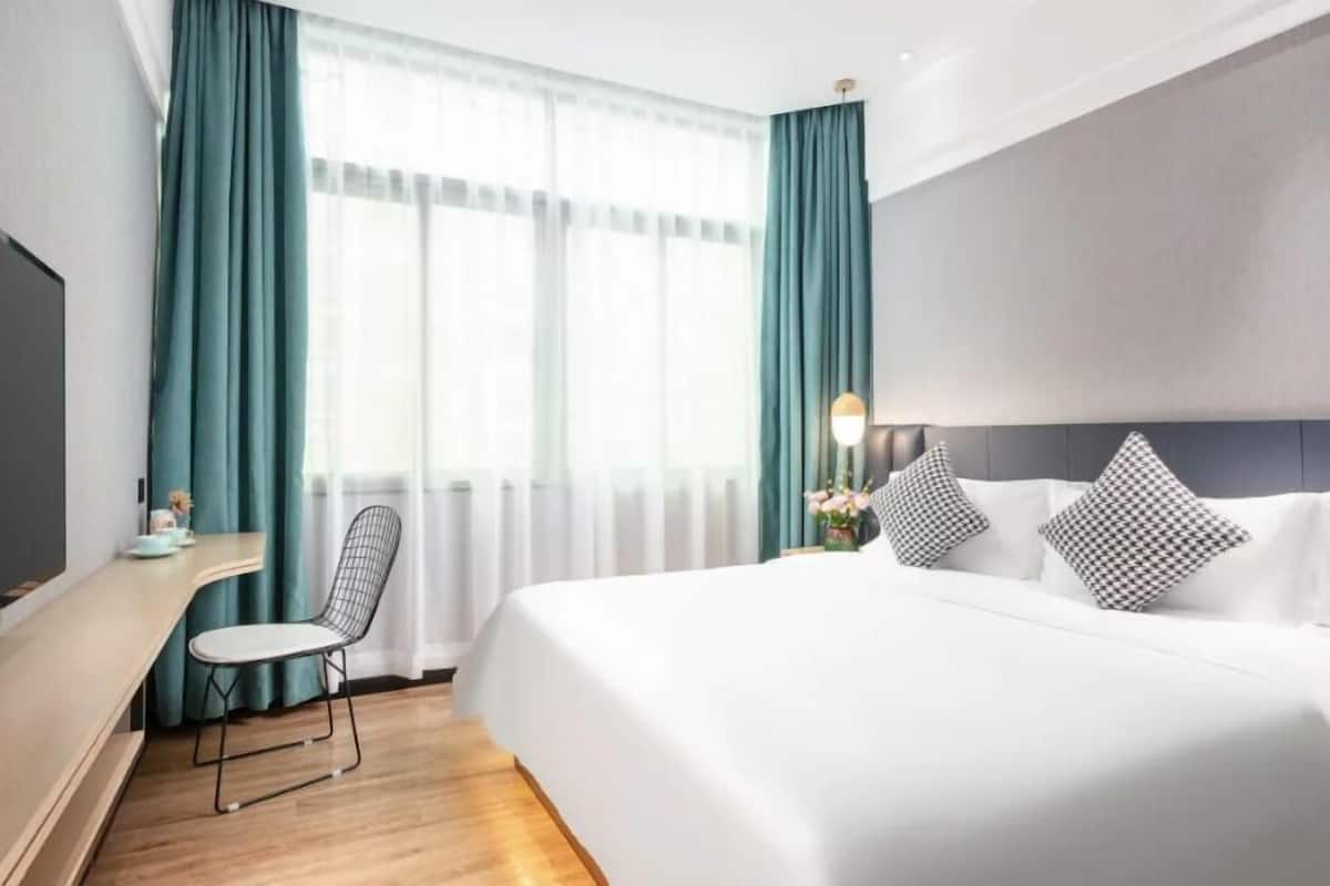 Ein Hotelzimmer mit einem Bett, einem Schreibtisch, einem Sessel und einem großen Fenster mit Vorhängen.