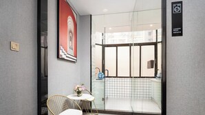Moderni hotellihuone, jossa on lasiovi, joka johtaa parvekkeelle, pieni pöytä tuoleineen sekä seinällä oleva kehystetty taulu.