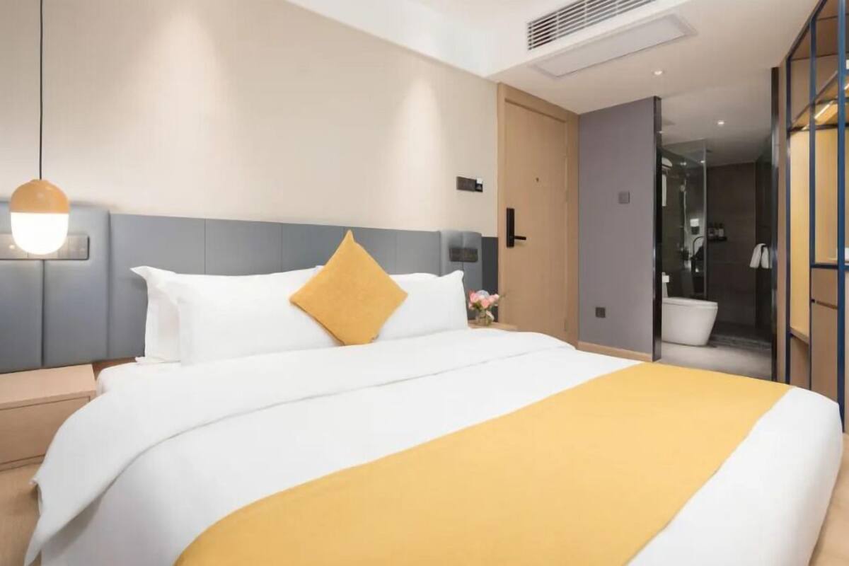 Ein modernes Hotelzimmer mit einem großen Bett, einem Nachttisch, einer Wandlampe und einem durch eine offene Tür einsehbarer Badezimmer.