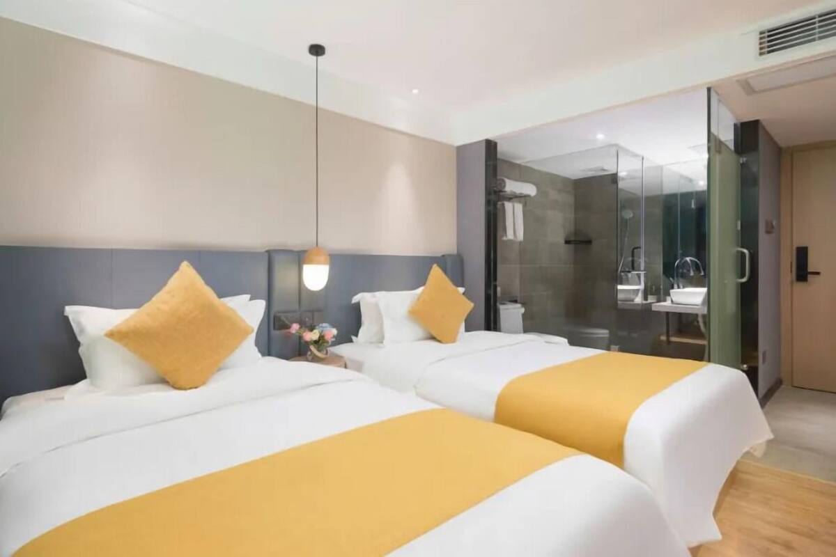 Ein Hotelzimmer mit zwei Betten, einer Duschkabine und einem durch eine Glastür einsehbaren Badezimmer.
