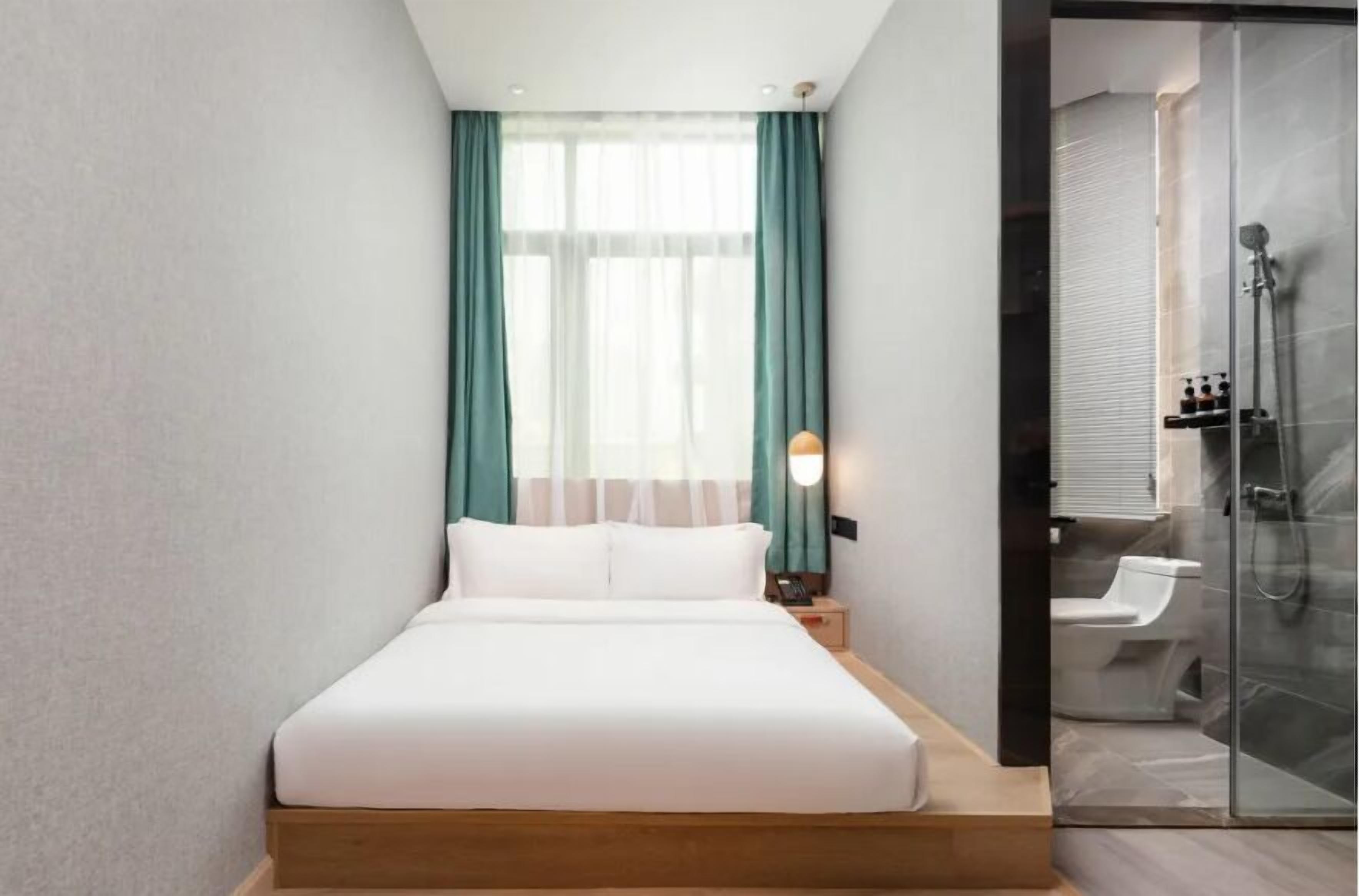Una habitación de hotel moderna con una cama grande, cabina de ducha de vidrio y una ventana con cortinas color turquesa.