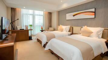 Quarto de hotel com duas camas, uma escrivaninha com computador, televisão e uma janela grande com cortinas.