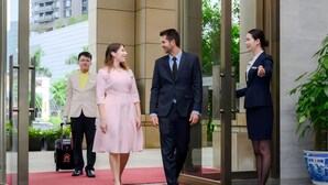 A hotel entrance with a red carpet, a glass door, and a receptionist.