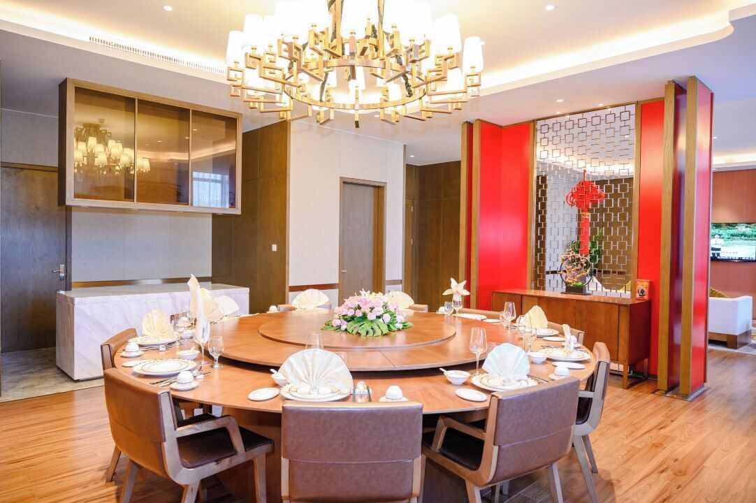 A modern dining area with a round table set for six, a chandelier, and a decorative wall panel.