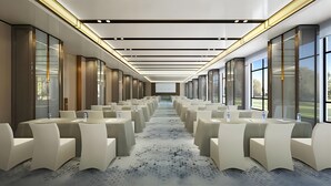 A modern conference room with rows of white chairs, a large screen at the front, and large windows on the sides.