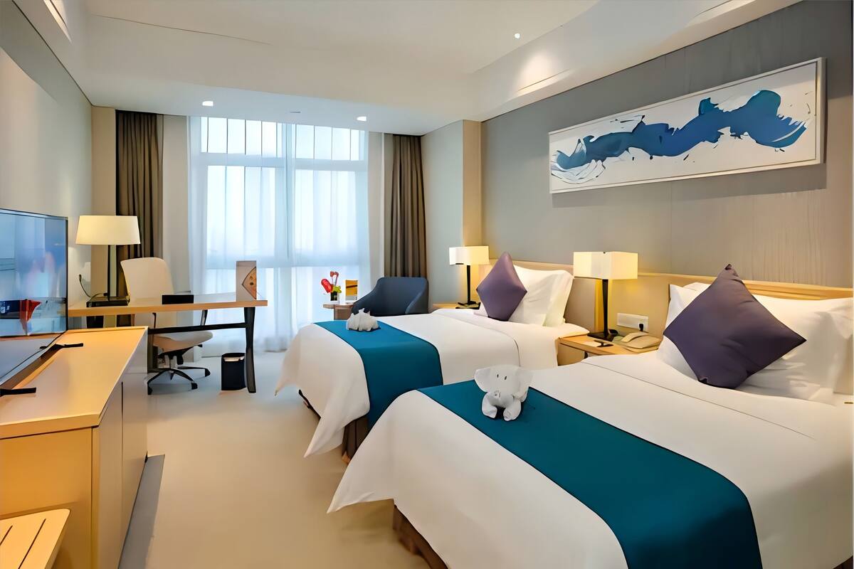 A hotel room with two beds, a desk with a computer, and a large window.