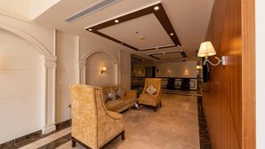 A lobby with a sofa and armchairs, marble flooring, and a wooden reception desk. - Holiday Plus Al Nuzha (Jeddah)