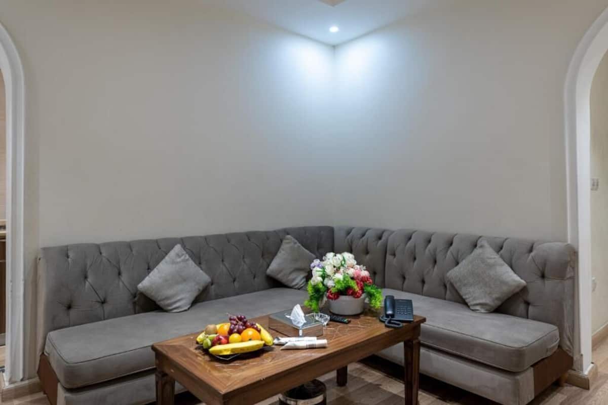 A living room with a grey sofa, a wooden coffee table with fruits and a vase of flowers, and a remote control.