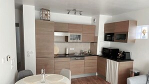 A modern kitchen with wooden cabinets, a built-in microwave, and a dining area with a round table and chairs. - Appartement Cosy au Centre de Meaux (Meaux)