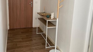 A hallway with a wooden door, a white shelf with a vase and a small plant, and a wall-mounted wooden rack. - Appartement Cosy au Centre de Meaux (Meaux)