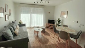 A modern living room with a grey sofa, a coffee table, and a dining area with chairs and a small table. - Appartement Cosy au Centre de Meaux (Meaux)