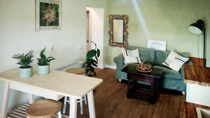 Una sala de estar con una mesa de comedor, un sofá y una mesa de centro. Hay plantas en macetas sobre la mesa y un espejo en la pared.