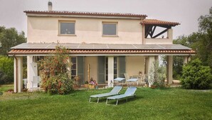 Una casa de dos pisos con un porche cubierto, paneles solares y un césped cuidado con sillones de descanso.