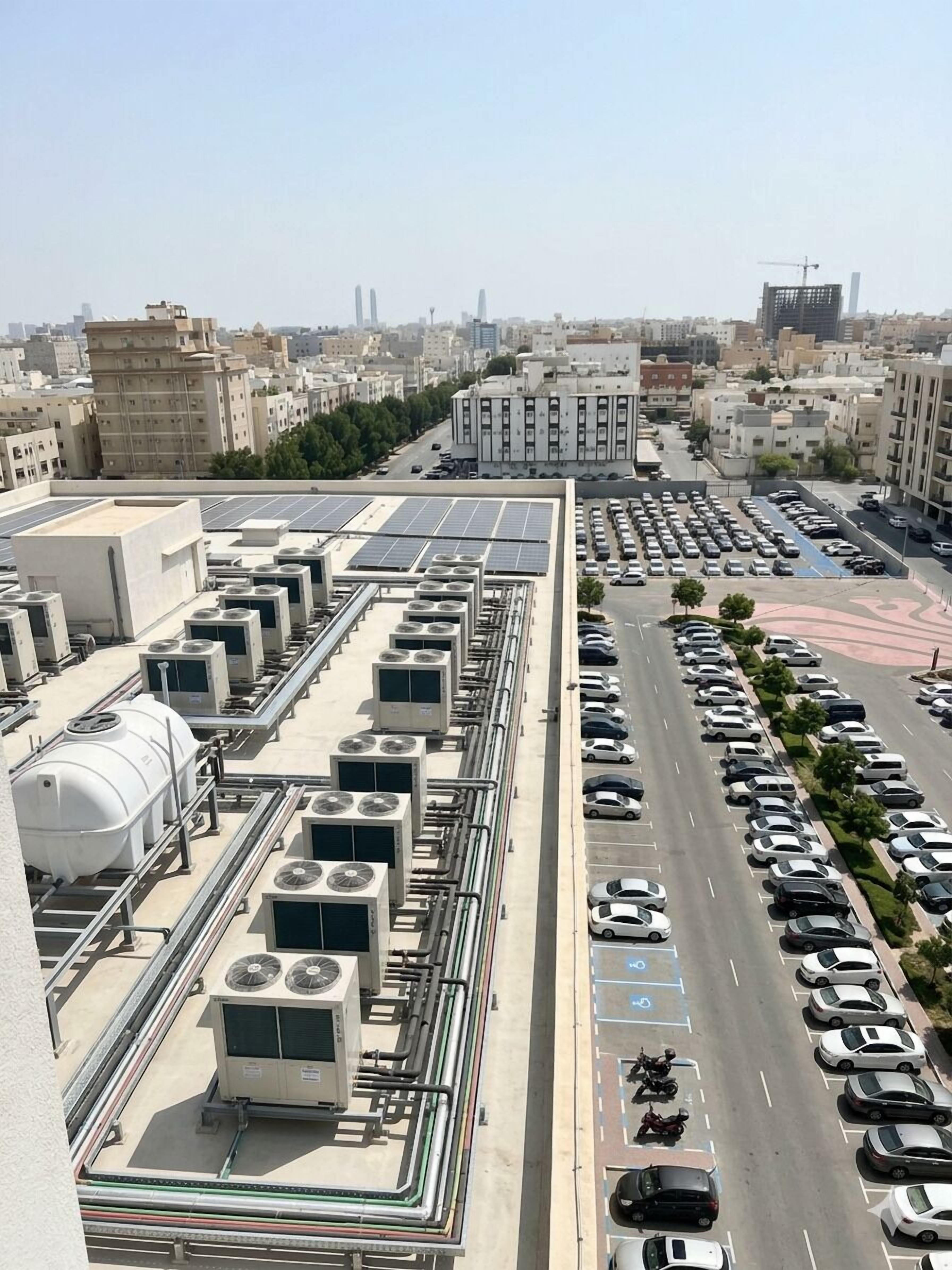 A rooftop with multiple air conditioning units and a parking lot with cars.