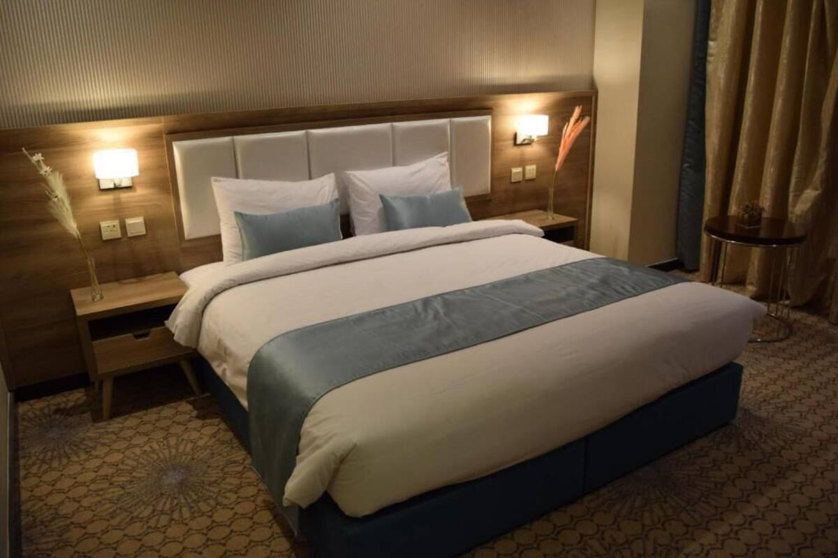 Une chambre d’hôtel avec un grand lit, deux tables de chevet, une petite table et une lampe fixée au mur.
