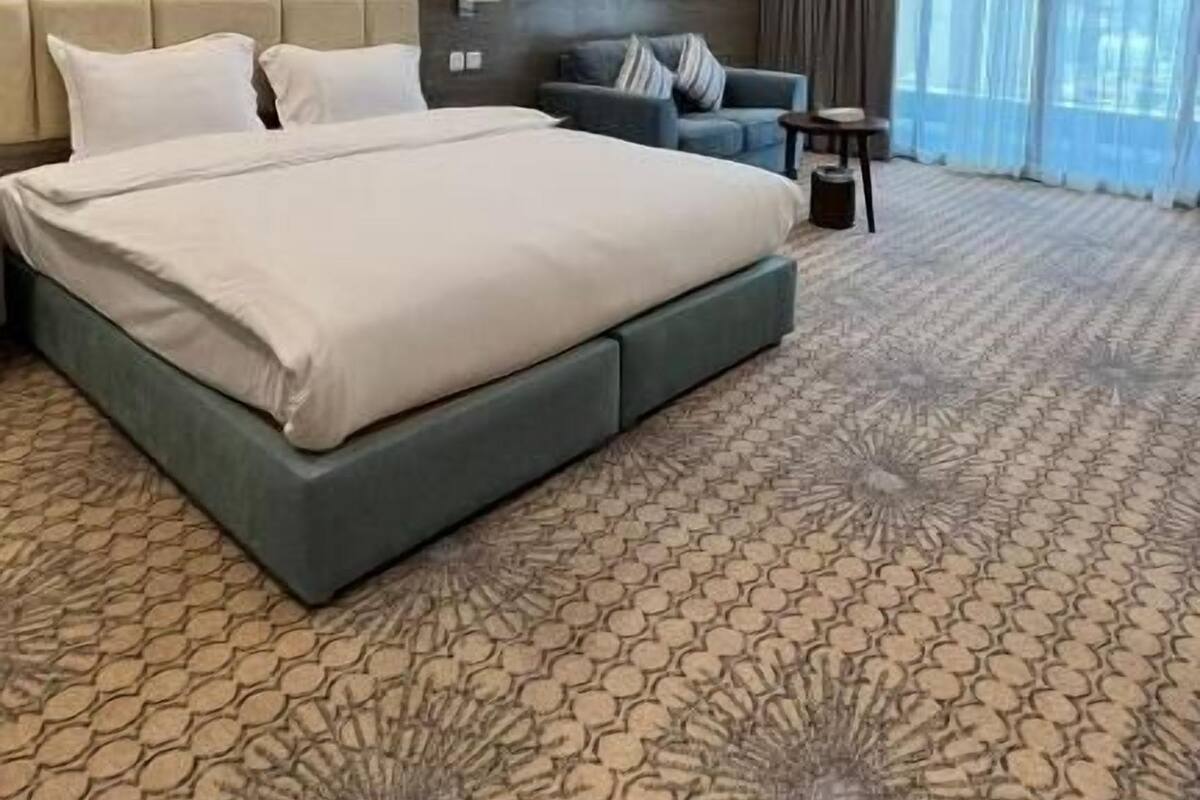 Une chambre d’hôtel moderne, dotée d’un grand lit, d’un canapé, d’une petite table et offrant une vue sur l’extérieur grâce à de grandes fenêtres.