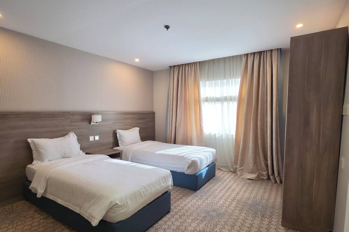 Une chambre d’hôtel avec deux lits, une moquette à motifs, une tête de lit et une fenêtre avec des rideaux.