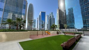 A modern urban plaza with high-rise buildings, green lawns, and benches. - Spectacular Views 1BR Apt Business Bay (Dubai)
