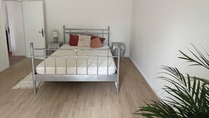 A minimalist bedroom with a metal bed frame, a bedside table, a hanging lamp, and a potted plant. - Apartment Chateau Rouge  (La Londe-les-Maures)