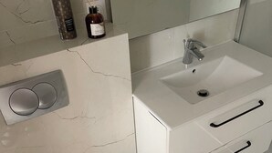 A modern bathroom with a white toilet, a sink with a mirror, and a small trash bin. - Apartment Chateau Rouge  (La Londe-les-Maures)