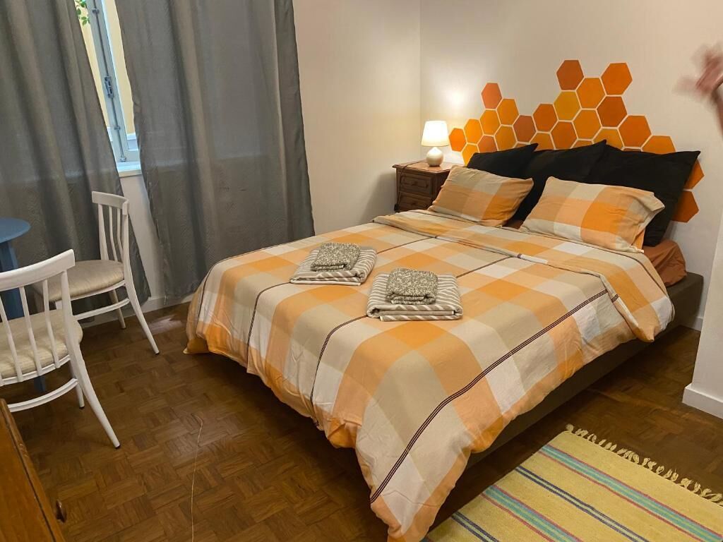 A bedroom with a checkered bedspread, a bedside lamp, a chair, and a window with curtains.