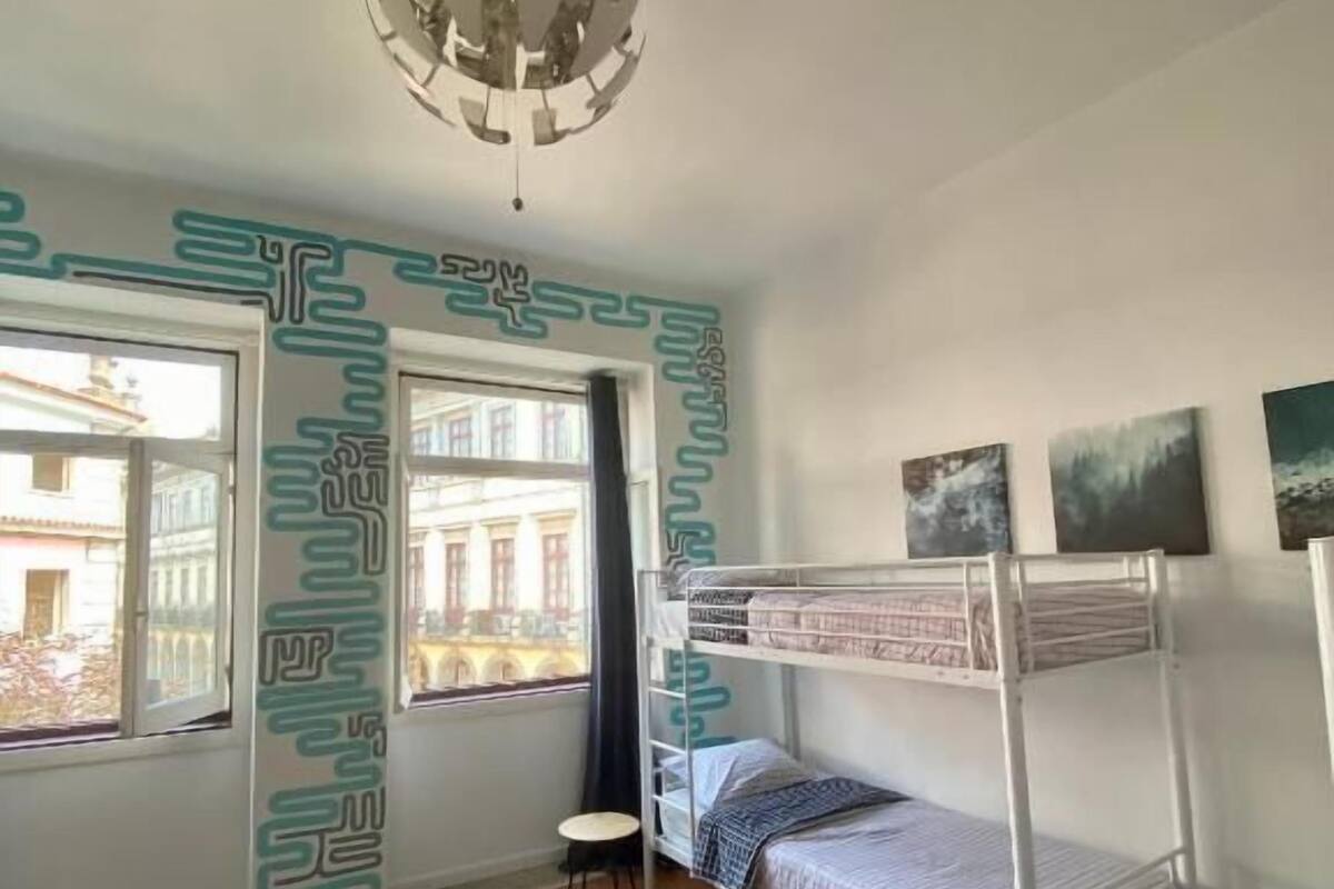 Une chambre avec un lit superposé, une petite table et une fenêtre donnant sur des immeubles.