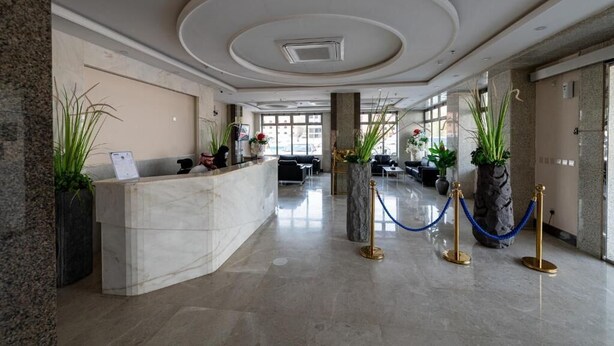 Eine Hotellobby mit einem Marmor-Rezeptionsschalter, Blumentöpfen, einer Sitzecke und einer blauen Absperrschlange.