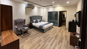 Ein modernes Hotelzimmer mit einem großen Bett, einem grau gepolsterten Sessel, einem kleinen Tisch, einem Kleiderschrank und einem Fernseher.