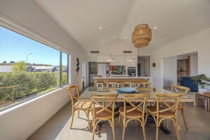 A modern kitchen with white cabinets, a central island, and a dining area with wicker chairs and a glass table. - Lake View Heights - Luxury large modern House (244 sq mtr) (Wanaka)