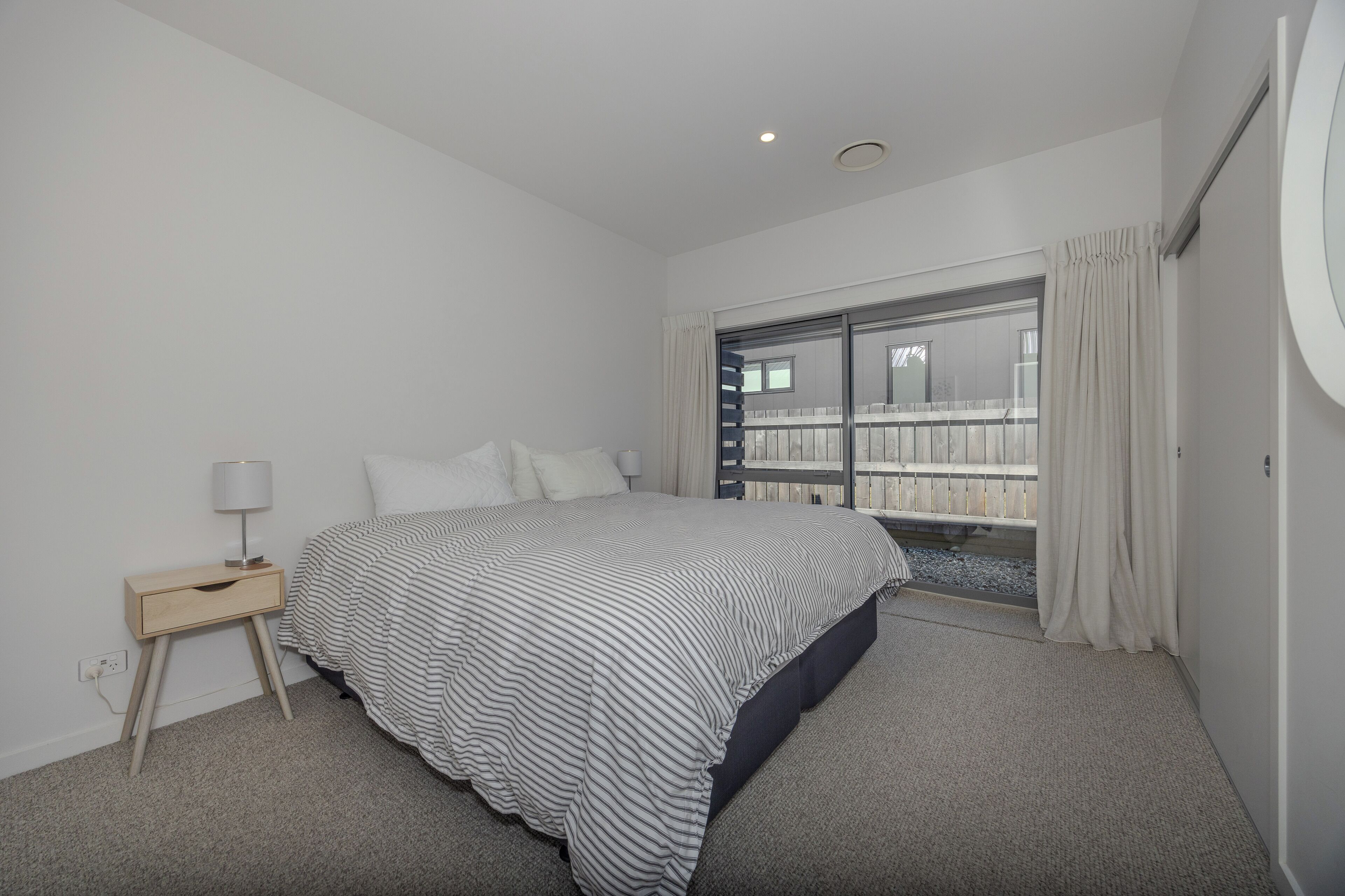Un dormitori amb un llit gran, una nitrera, una finestra amb cortines i vista a un balcó.
