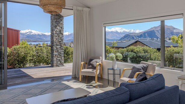 A modern living room with a stone pillar, large windows with mountain views, and a cozy seating area. - Lake View Heights - Luxury large modern House (244 sq mtr)  (Wanaka)